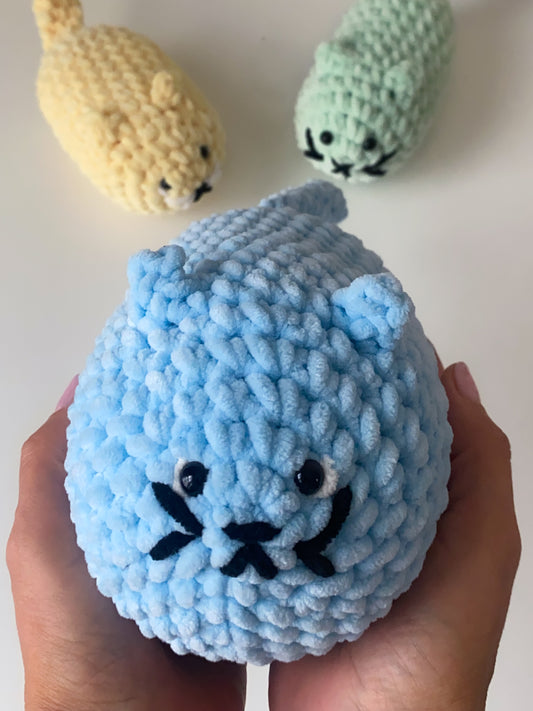 Blue knitted cat toy held in a hand with other cat toys in the background.